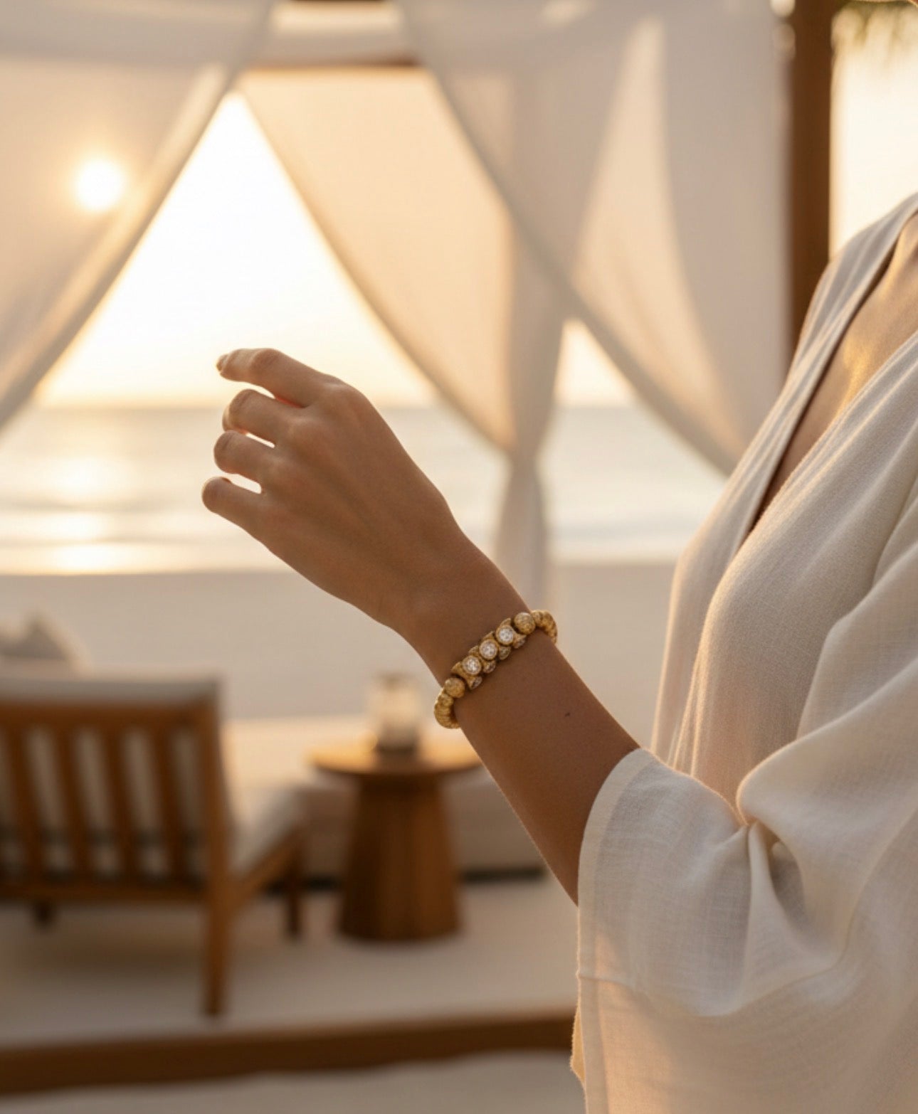 Woman wearing a handcrafted Limited Edition - Aurea Luminis gold and bead bracelet, glowing softly in warm natural light with a relaxed, beachside setting.