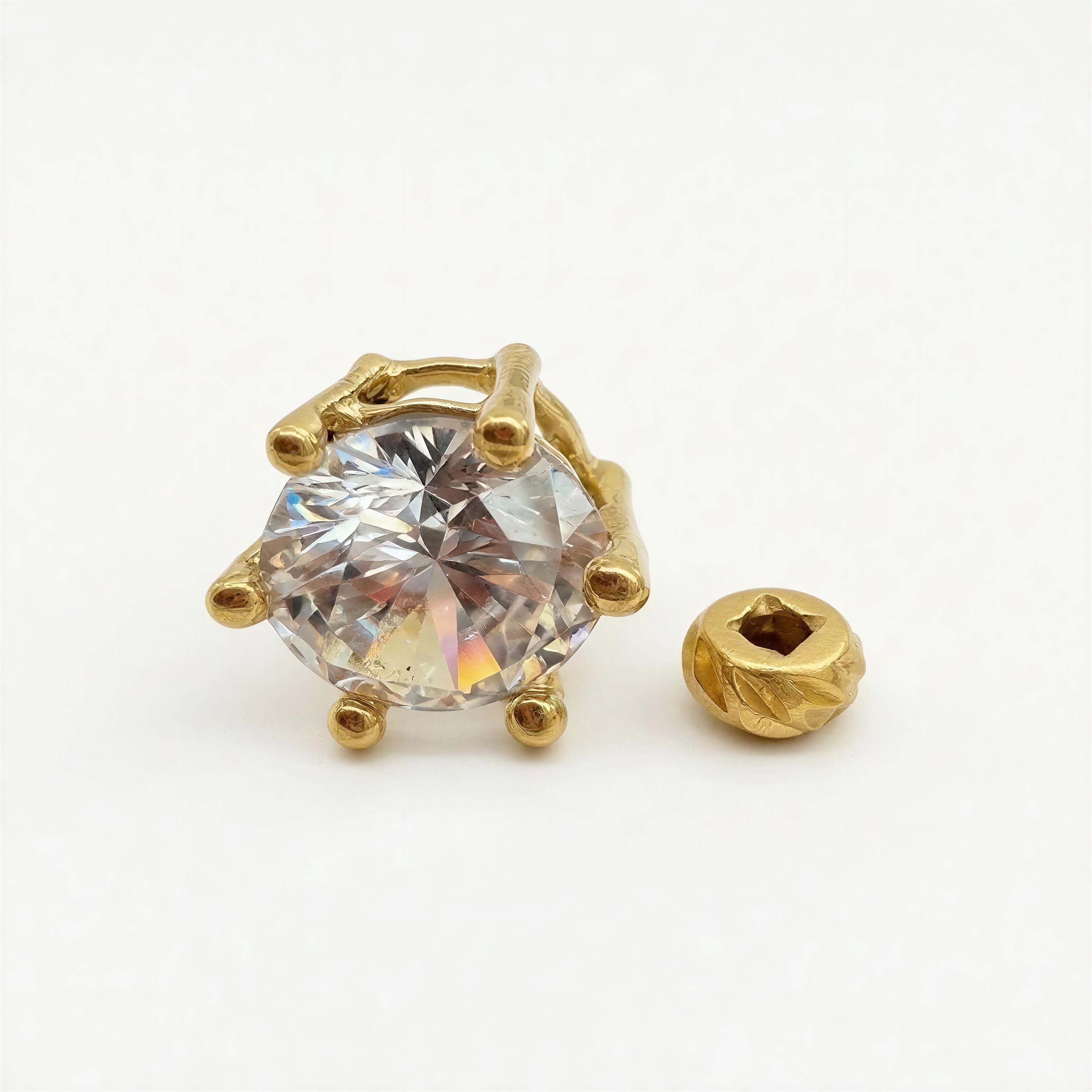 Close-up of a sparkling gemstone held by a unique gold setting next to a small intricately detailed gold bead, showcasing the design elements of the RING - Golden Radiance.