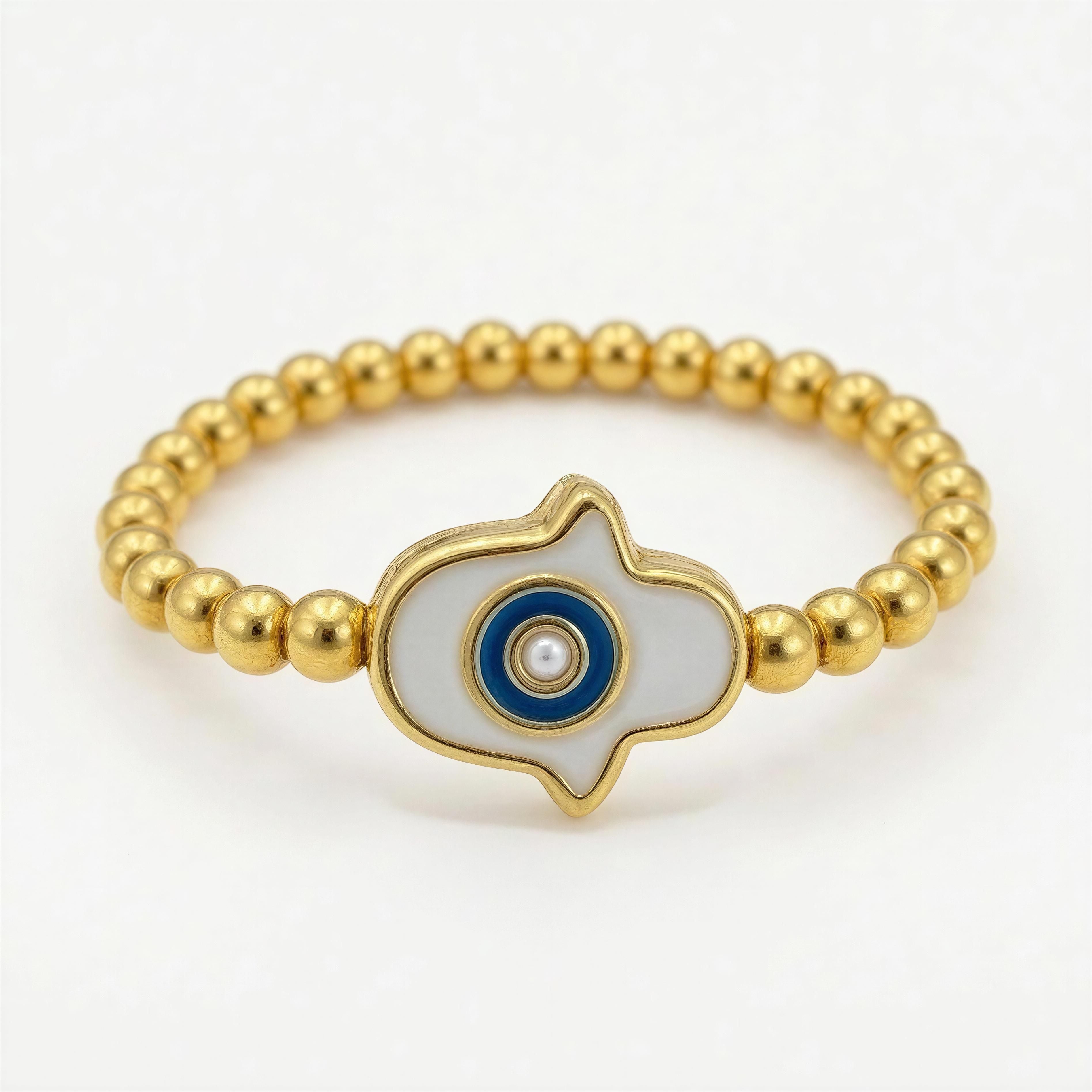 Gold beaded bracelet featuring a central white and blue enamel charm with a small pearl accent, showcasing the RING – Ojo de Luz design in handcrafted luxury jewelry style.