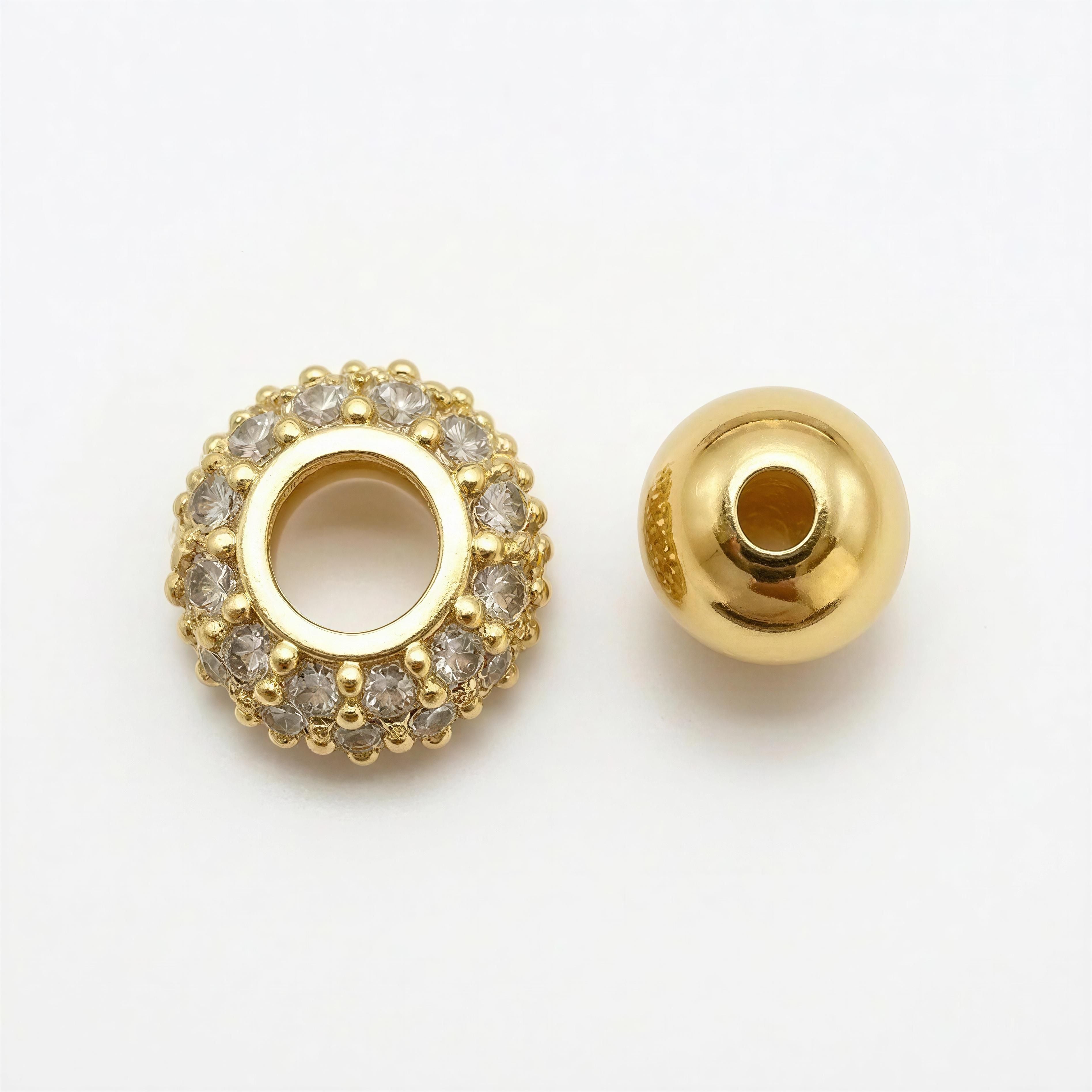 Two gold beads on a white background, one encrusted with small clear stones and the other smooth and polished, representing luxury handcrafted details from XX ÉLÉGANCE – Champagne Royale.