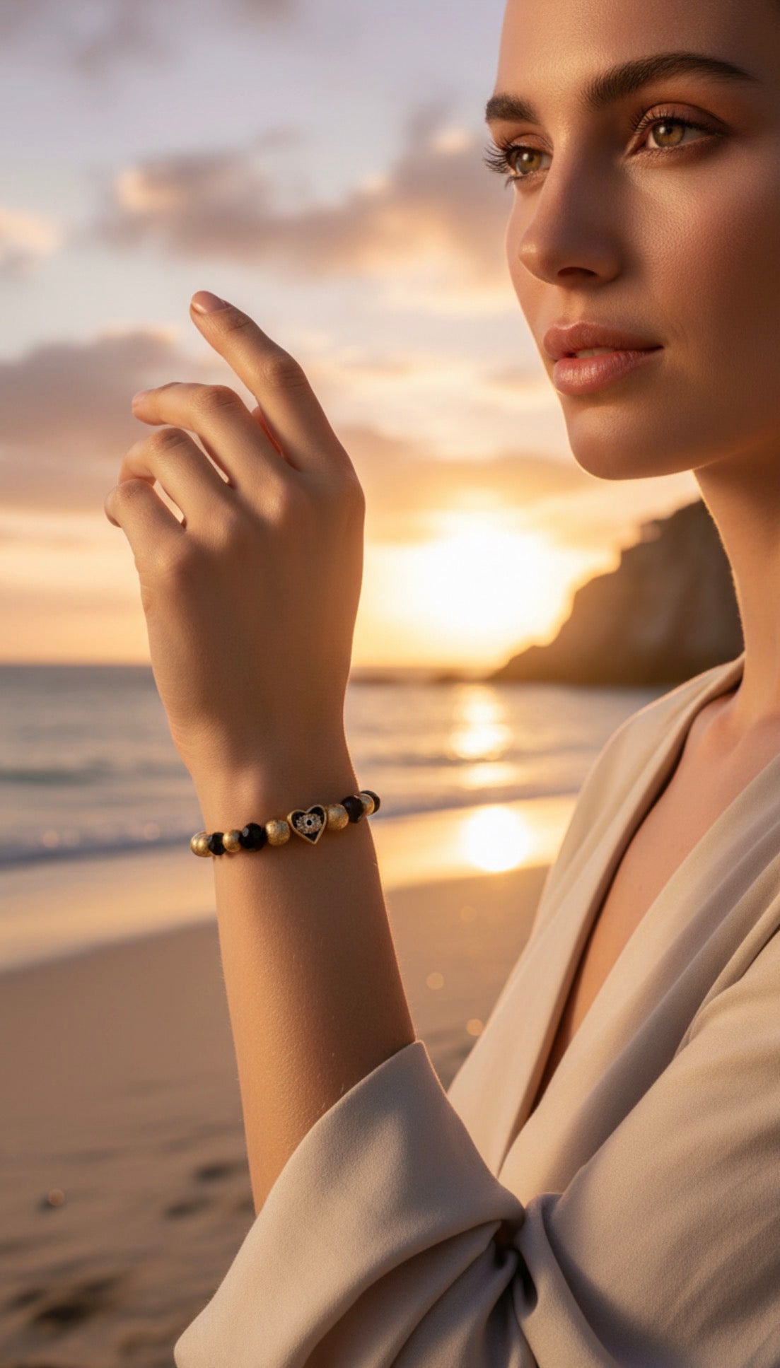 Close-up of a woman wearing the Timeless Collection - Aurea Cordis bracelet featuring gold leaf and dark beads, posed elegantly by the ocean at sunset.
