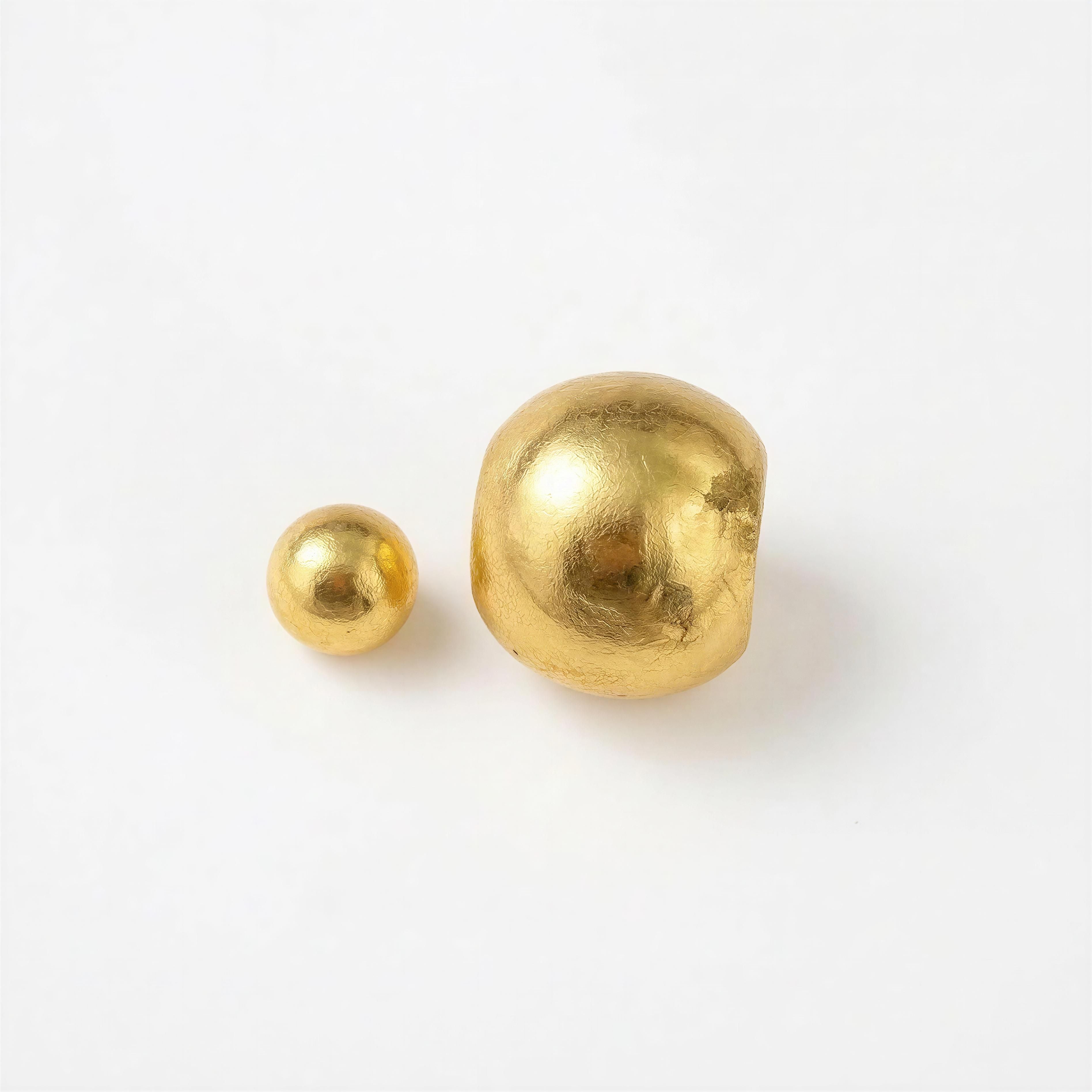 Close-up of two irregularly shaped gold beads on a white background, highlighting the handcrafted, luxurious design of the XX ÉLÉGANCE - Noir Clover collection.