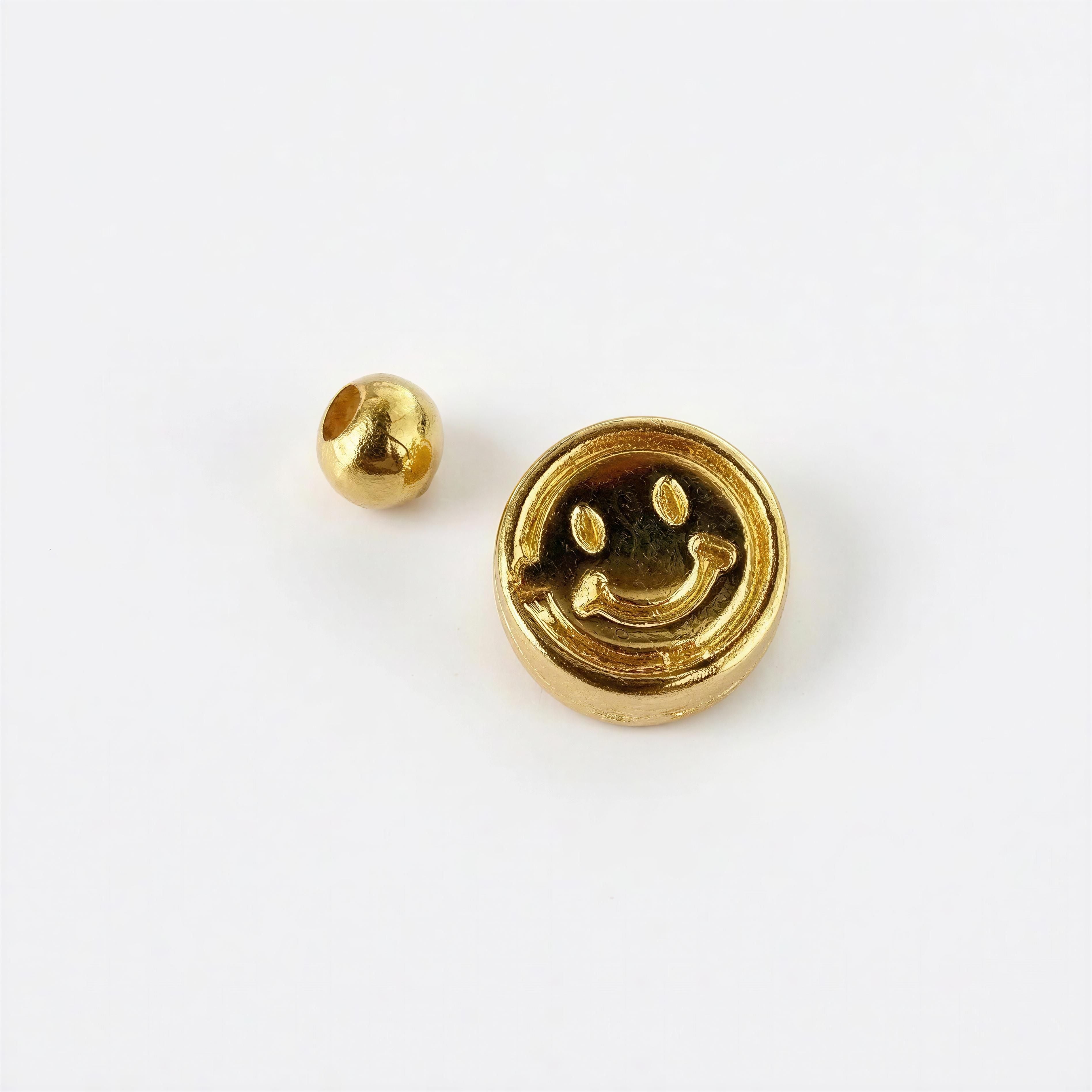 Close-up of a gold bead and a gold charm with a smiley face design for RING – Soleil Smile, showcasing handcrafted luxury jewelry elements.