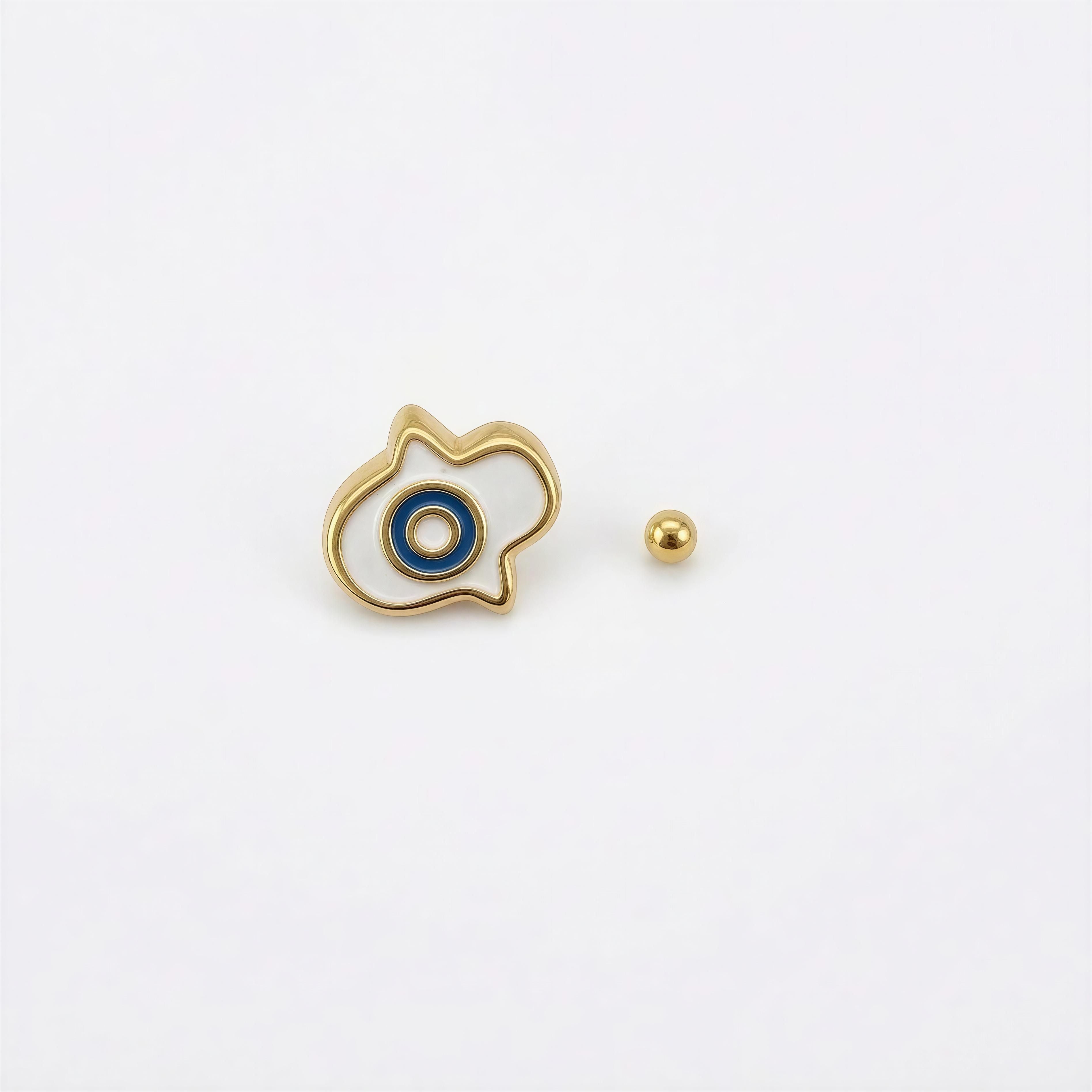 The Little Icon By Xenna Xava – Golden Eye featuring a delicate gold outline with a central blue and white enamel eye motif, accompanied by a small polished gold bead, reflecting handcrafted luxury jewelry design.