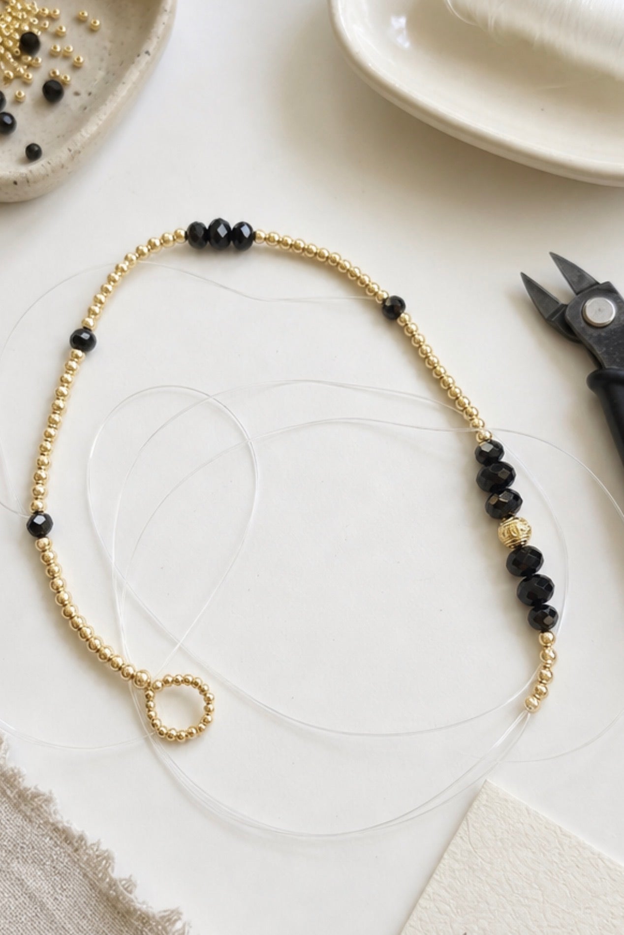 Delicate handcrafted luxury beaded chain with alternating gold and black beads, elegantly arranged on a white surface alongside crafting tools, featuring The Riviera Sunglass Chain — Limited Collection.