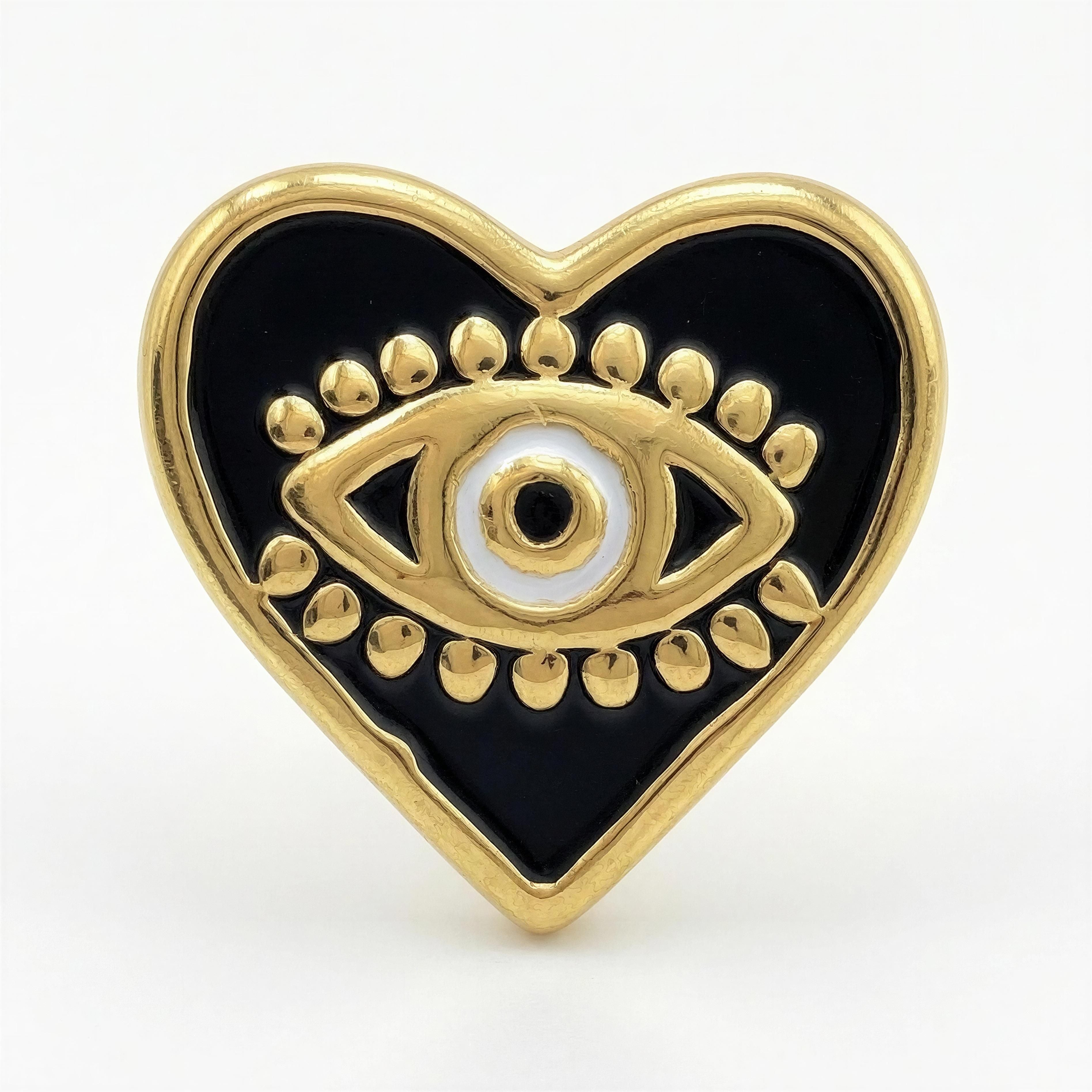 Heart-shaped black enamel pin with a gold eye design and decorative gold dots, part of the Timeless Collection - Aurea Cordis by Atelier X handcrafted jewelry.